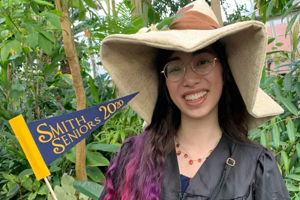 Isabelle Hodge holding "Smithie Seniors 2020" flag in the Lyman Conservatory and wearing a big hat