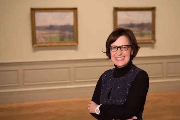 Kathy Galitz with her arms crossed smiling into the camera in an art gallery