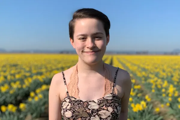 Kristina Chiu smiling in the foreground. In the background is a field of yellow flowers