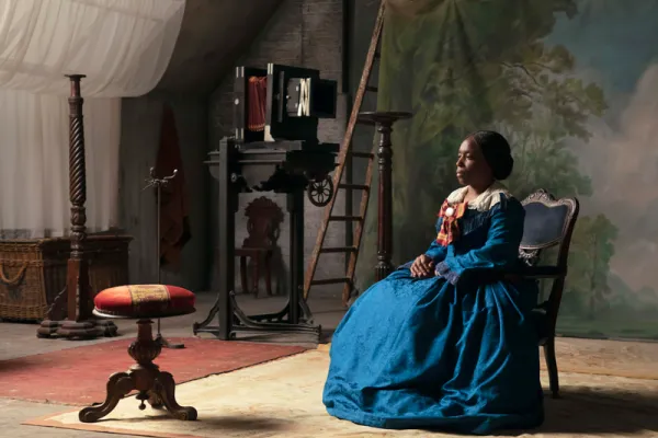 Color film still of a Black woman in 19th century clothing in a photo studio