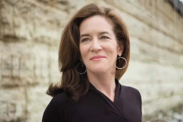 Nan Alexander Doyal against a stone wall, looking off into the distance with a half smile