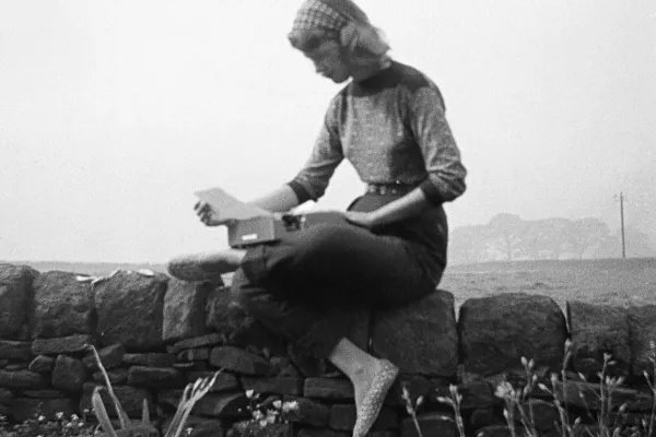 Sylvia Plath sitting on a stone wall with a typewriter on the Yorkshire moors, September 1956.