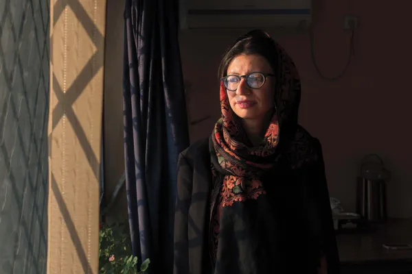 Sharharzad Akbar wearing a red and black head scarf with black glasses looking out a window