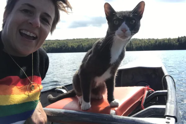 Winter Miller in a rainbow shirt with a gray and white cat on a boat in a lake.