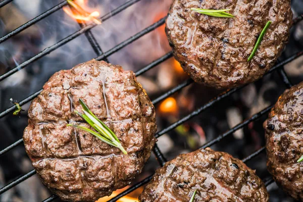 Four hamburger patties cooking on an outdoor grill