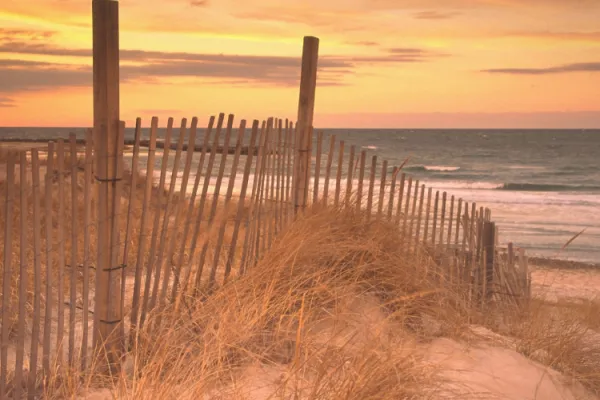 A beach at sunset with a dilapidated fence in the foreground