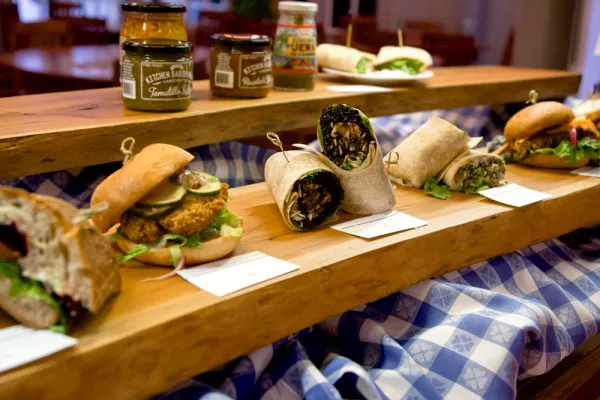 Row of sandwiches and wraps on a wood shelf with condiments on another shelf behind and above