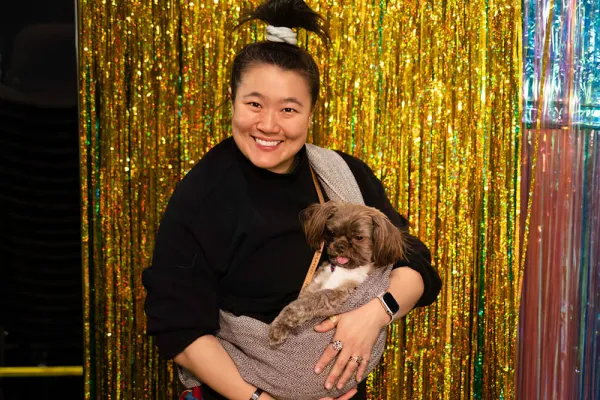 Theater artist Diana Oh holds their dog shovels against a backdrop of shimmering beaded curtains