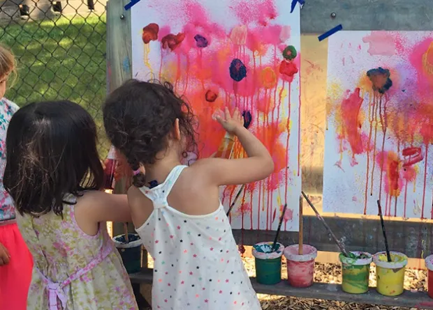 Three girls painting pictures of red flowers