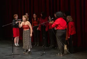 Singers on stage, performing, in front of a red curtain
