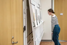 A student reading poster presentations that are leaning on a shelf on a wall