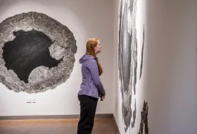 A student in the Smith Art Museum, staring intently at artwork on the right-hand wall