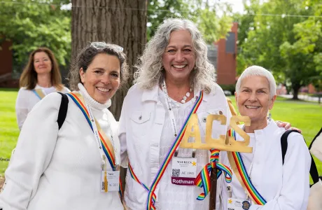 Ada Comstock Scholar alums wear white with rainbow-colored sashes and smile at the camera during Reunion