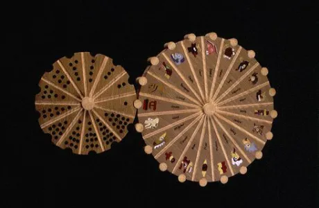 Two wooden circular objects with radial patterns are displayed. The larger wheel features astrological symbols, while the smaller one shows arranged black dots.