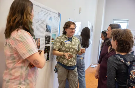 A student holds a rock sample while explaining their poster presentation