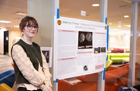 A student smiles at the camera next to their poster presentation