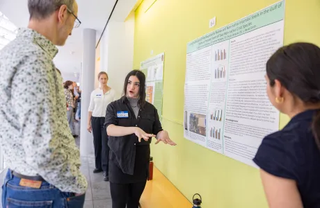 A student explains their poster presentation at Collaborations