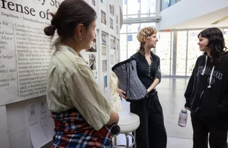 A student holds up a handmade corset, part of their Collaborations presentation