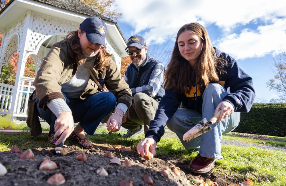A student and parents plant garlic bulbs near the Capen gazebo