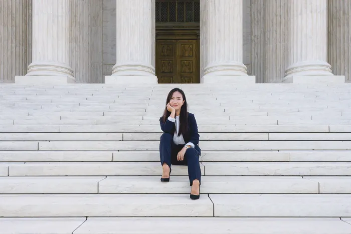 A student sitting on the steps of the Supreme Court in a suit.
