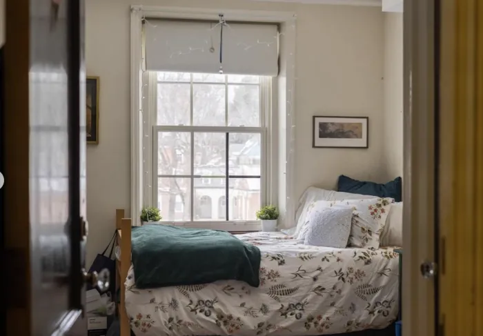 A cozy bed in Emerson House, next to a window.