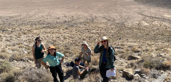 Five people on a desert hillside smiling into the camera