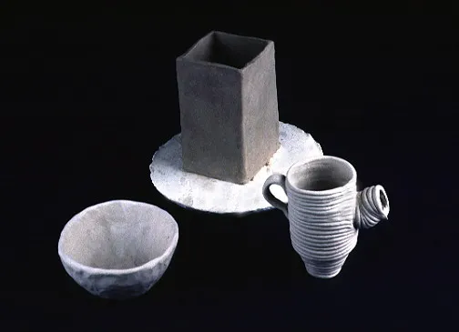 Ceramic art pieces, including a square vessel on a circular slab, a simple bowl, and a textured mug with a handle