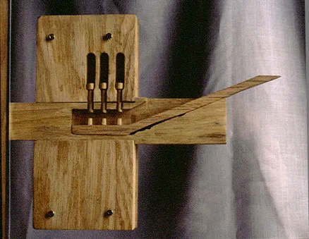 A wooden mechanical sculpture features vertical bars and a long lever
