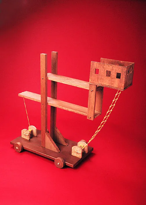 Wooden catapult model features beams, a basket on the end, rope details, and wheels