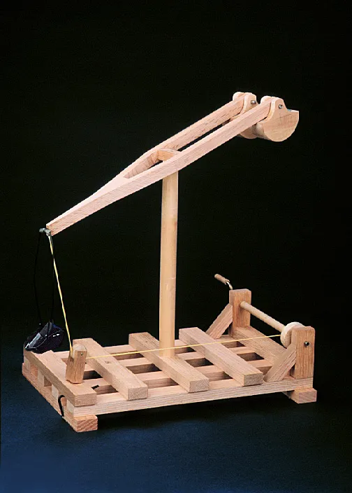 A wooden mechanical model with a geared lifting arm is displayed on a grid-like base, demonstrating basic engineering principles