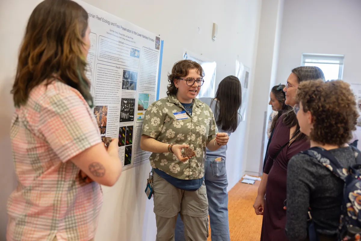 A student holds a rock sample while explaining their poster presentation