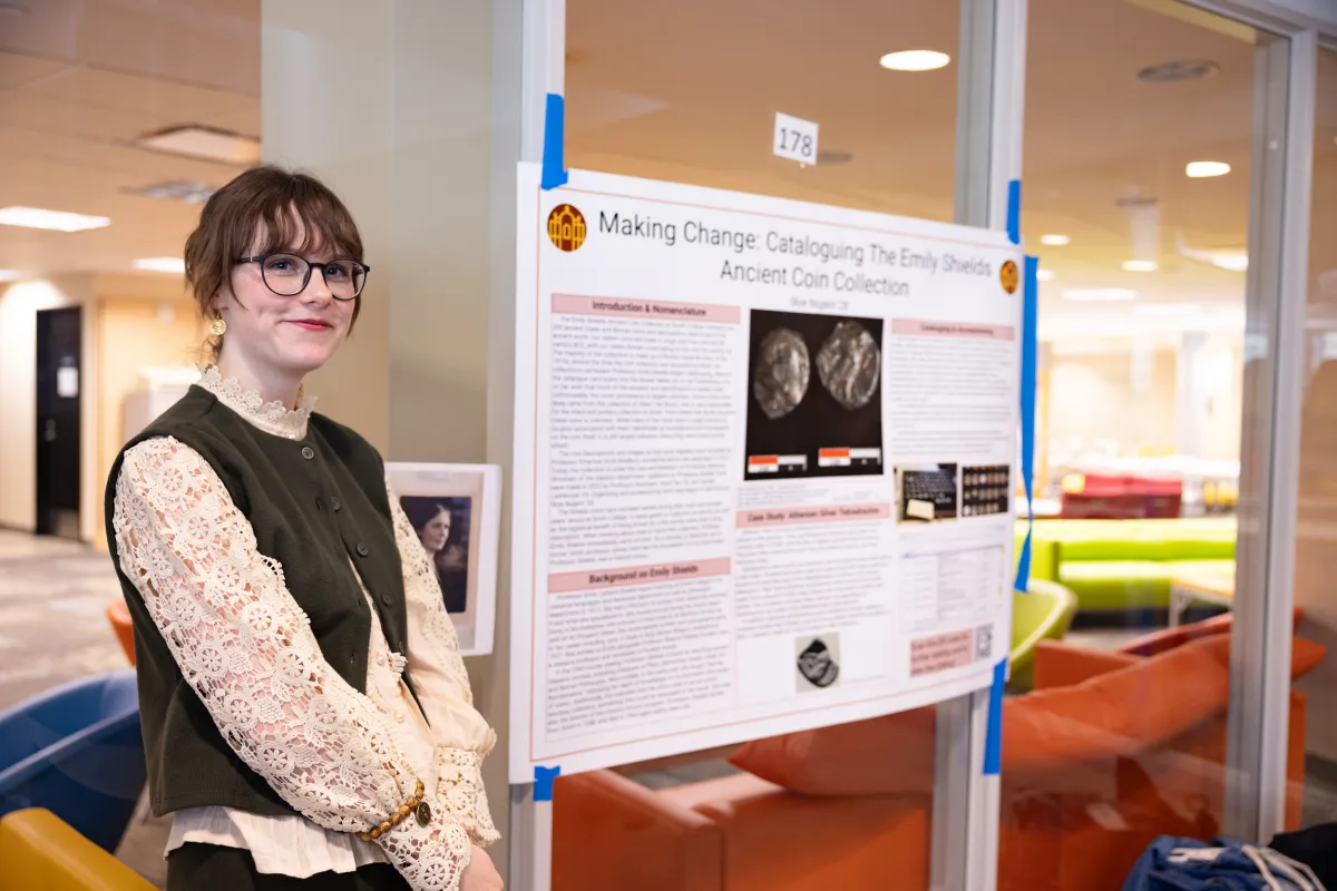 A student smiles at the camera next to their poster presentation
