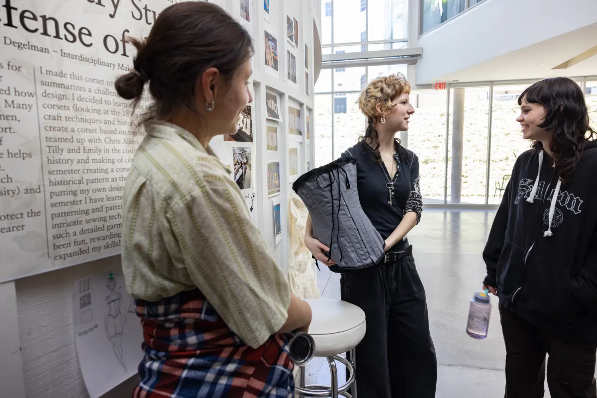 A student holds up a handmade corset, part of their Collaborations presentation