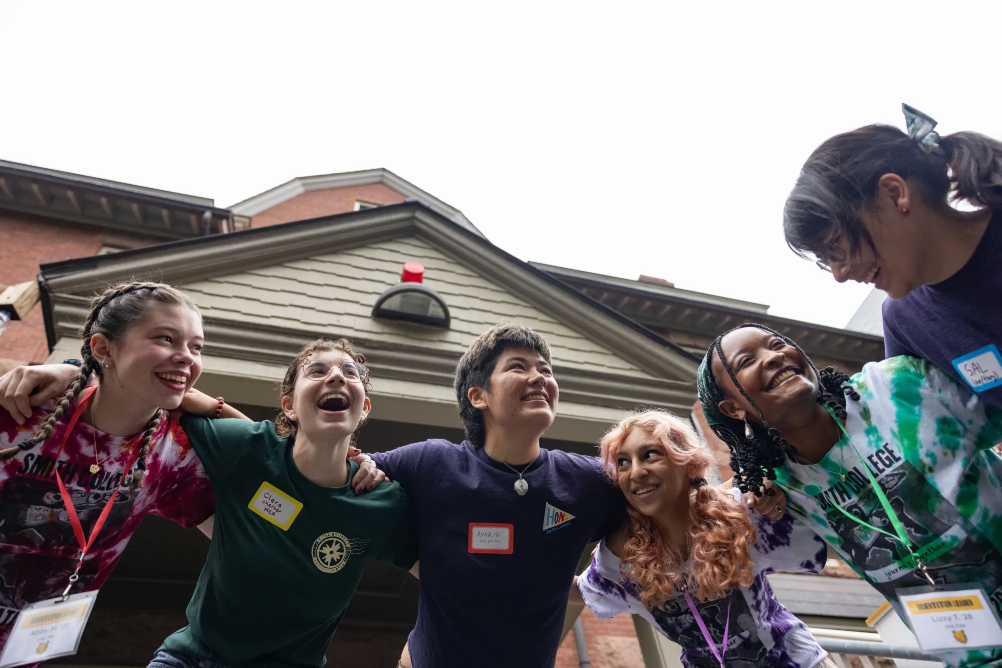 Student leaders, many in tie-dye shirts, laugh and smile at each other with their arms draped around one another's shoulders