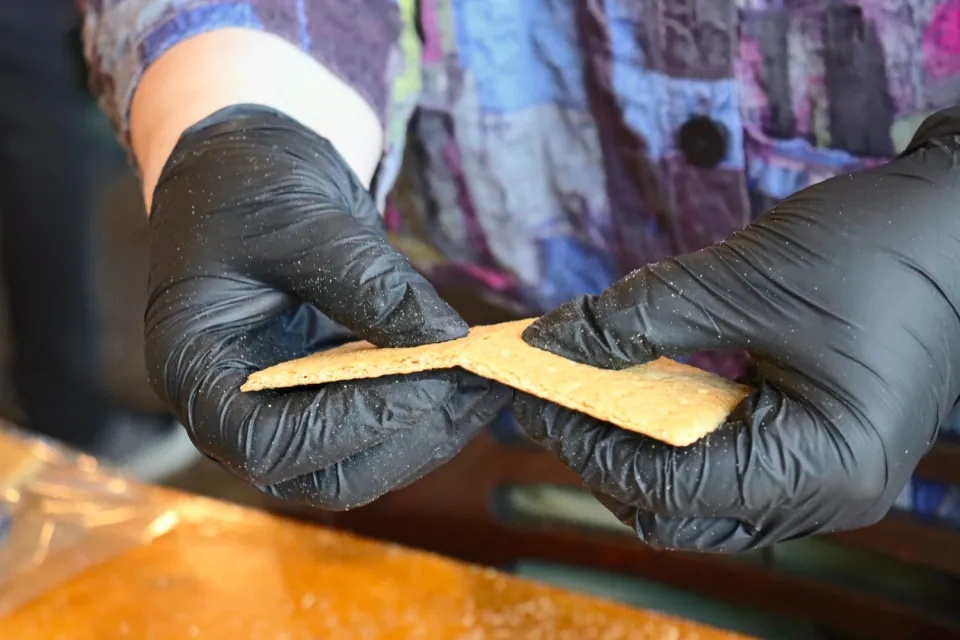 A photo of a pair of gloved hands snapping a graham cracker in half.