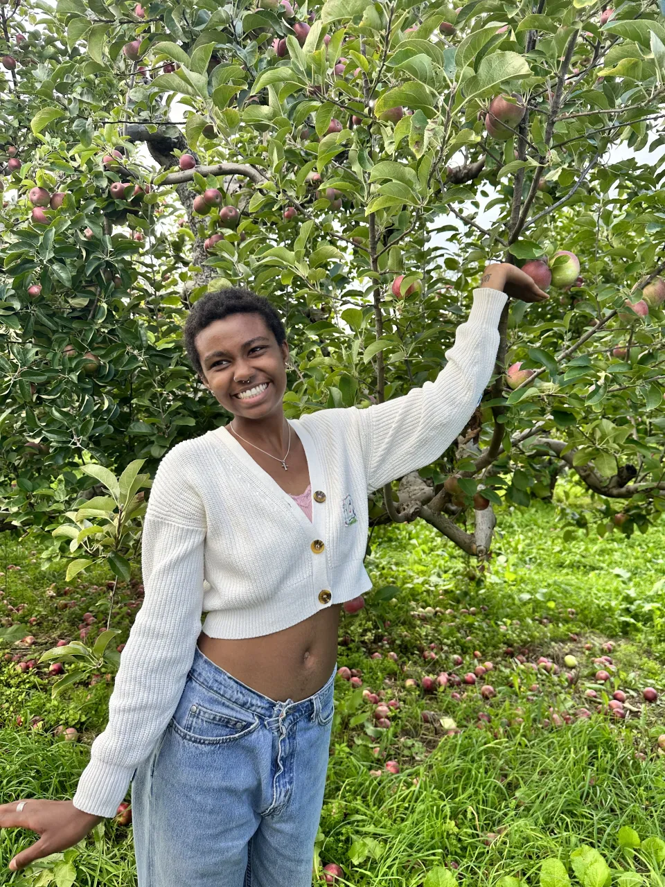 Mack Case '24 reaches for an apple in an orchard, smiling