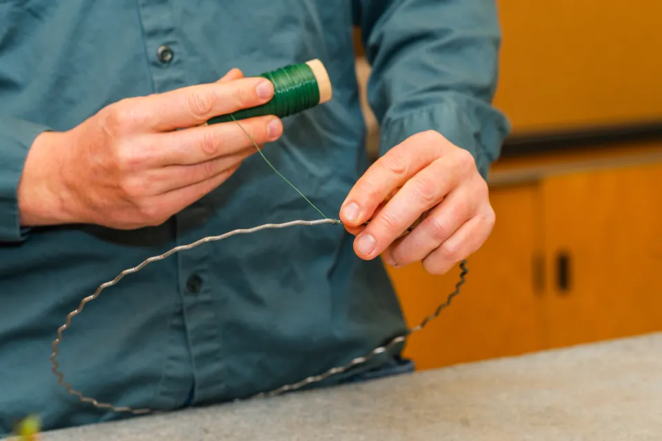 Dave Dion's hands as he winds green wire around a wreath ring