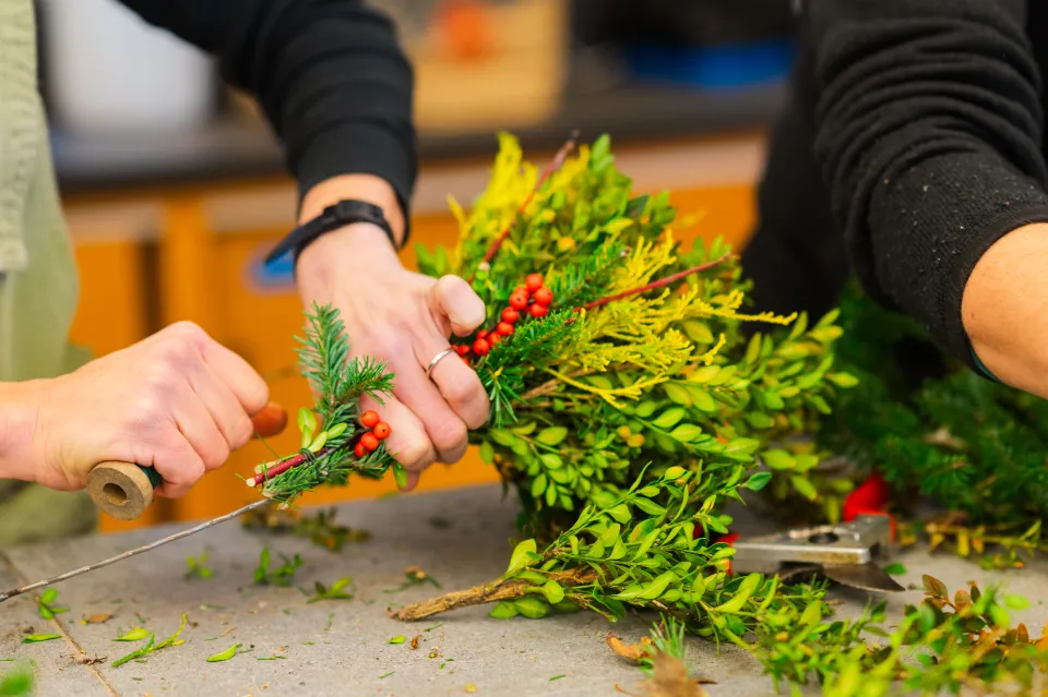 Julie Thomson's hands as she winds green wire around a wreath ring and evergreen bundle with winterberries