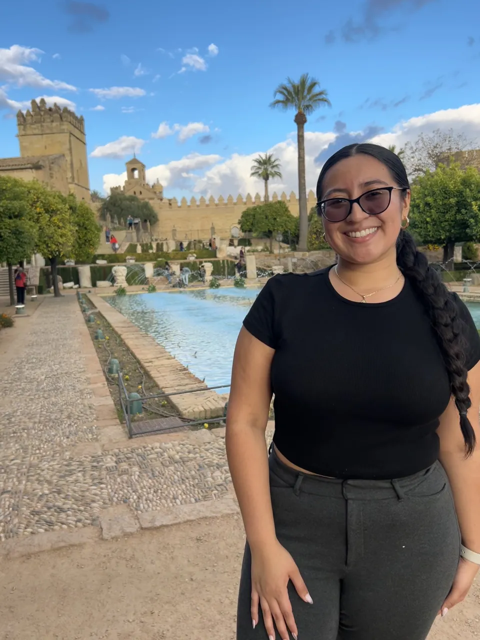 Michel Ruiz-Fuentes ’24, smiling, stands outside in front of a swimming pool with palm trees behind
