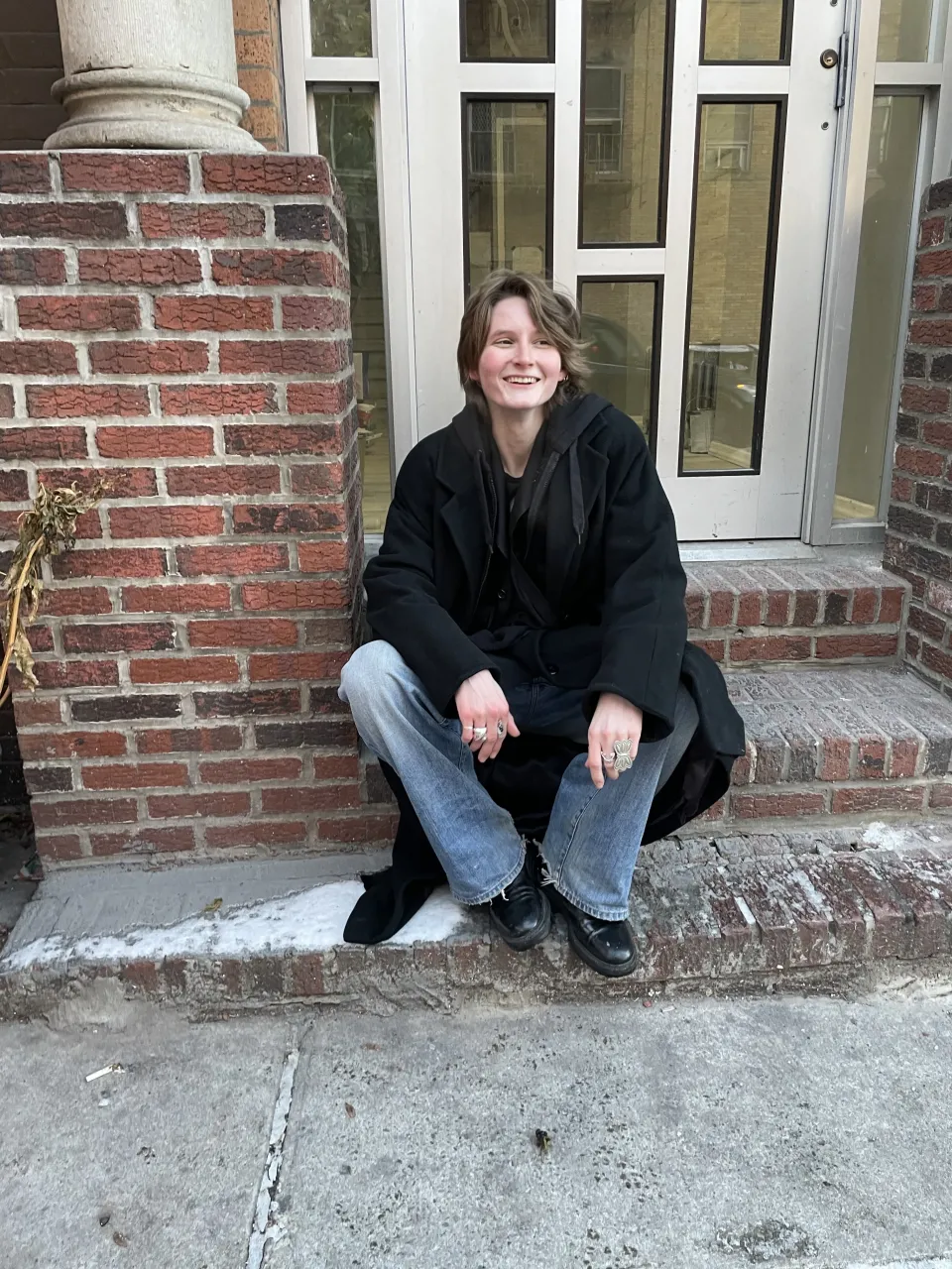 Henne Van Campen ’24 in a black jacket laughing on a brick stoop