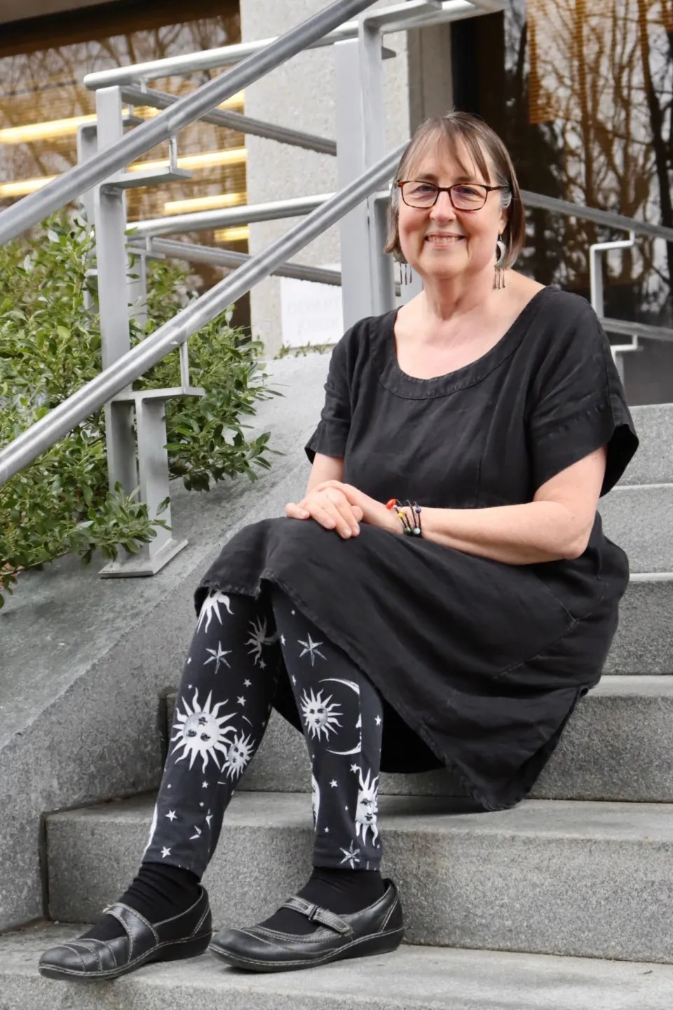 Meg Thacher sits on stairs wearing black and white sun and moon leggings