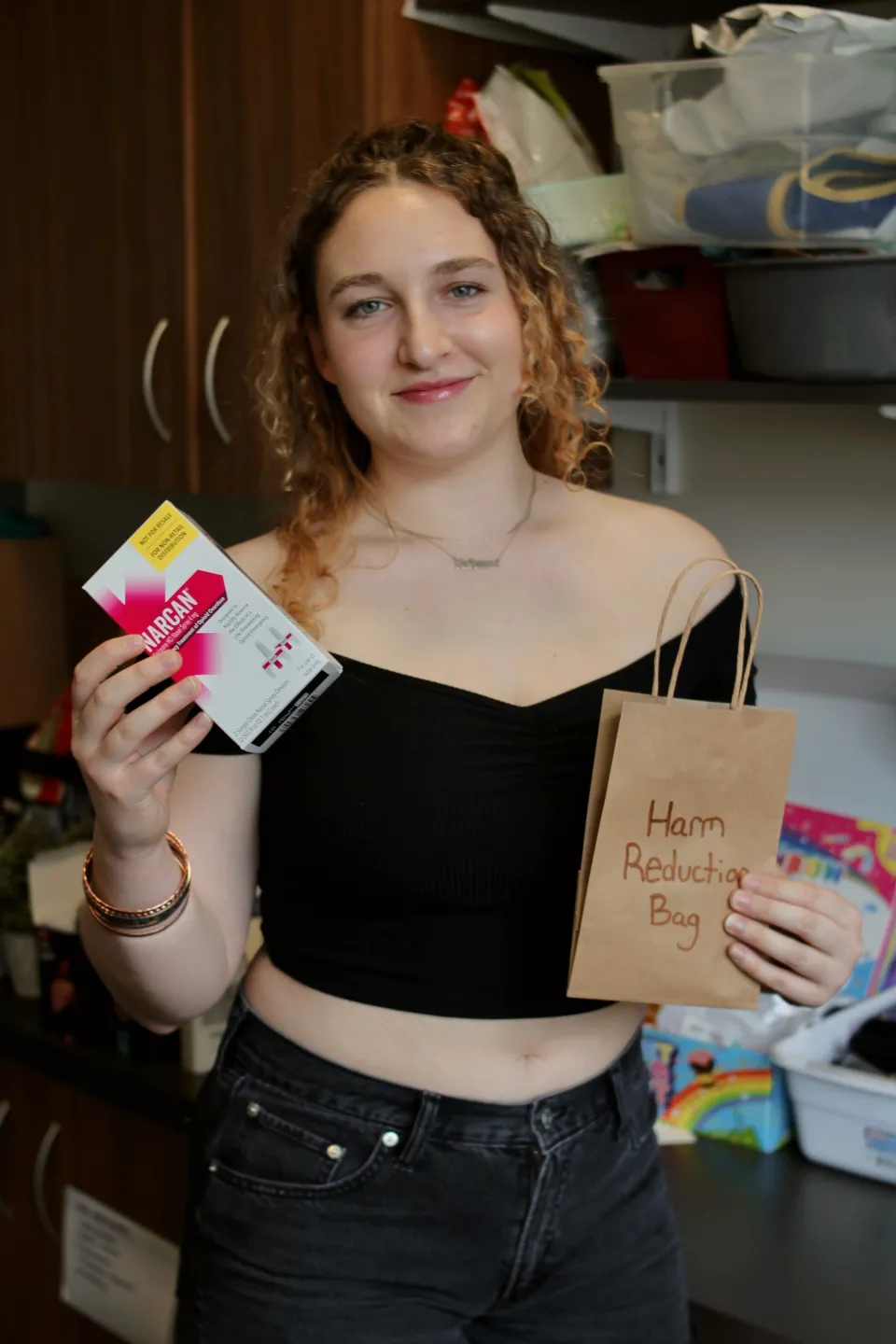 Cailin Young ‘24 prepares a harm reduction bag in the Schacht Center, holding up Narcan and smiling