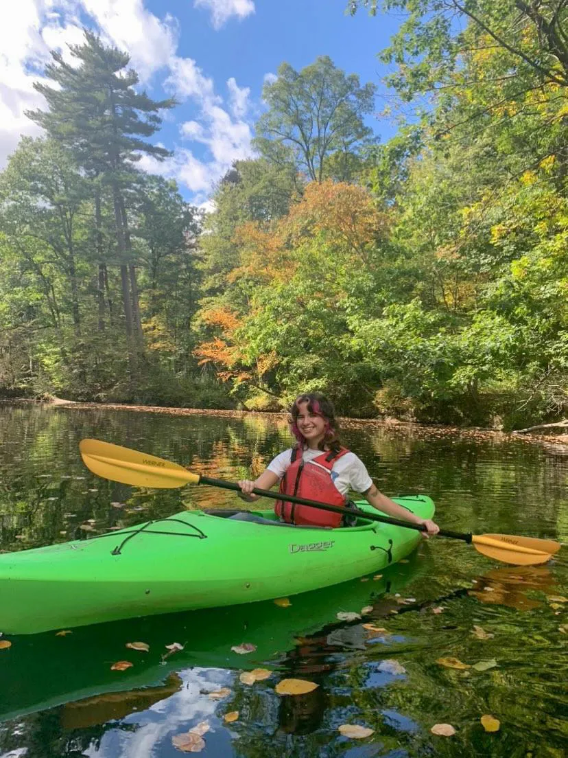 Ciana Socias in a green kayak with a yellow paddle and red lifejacket on Paradise Pond in the fall