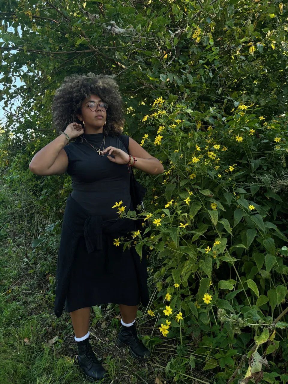 Kim Estrada in a black dress outside in greenery near a spray of small yellow flowers