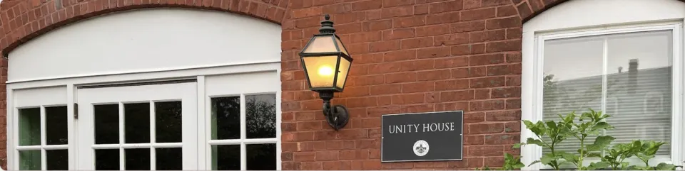 The Unity House plaque - white text on black with the seal beneath, displayed on the former carriage house, a brick building with white accents and ironwork light fixtures.