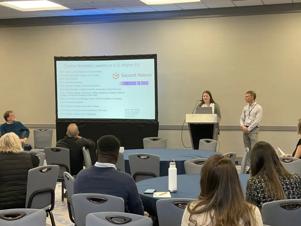 Emma Larsen presents research to a group while Alex Barron looks on.