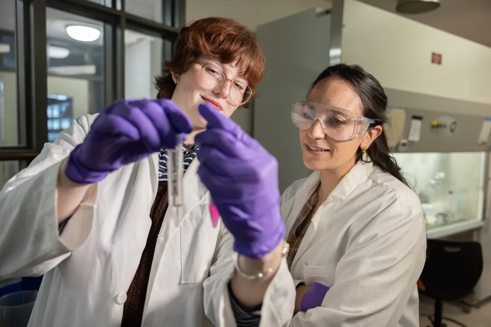 Professor Tanya Lama on left watches as her student prepares a test tube in Lama's genomic lab at Smith.