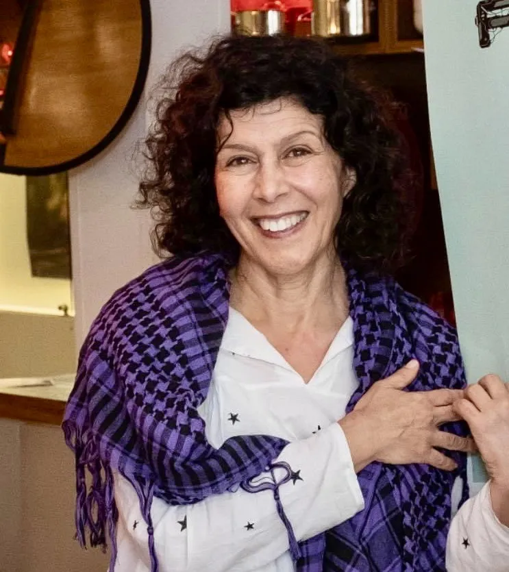 Portrait of filmmaker and writer Alia Yunis smiling while wearing a purple-and-black keffiyeh scarf.