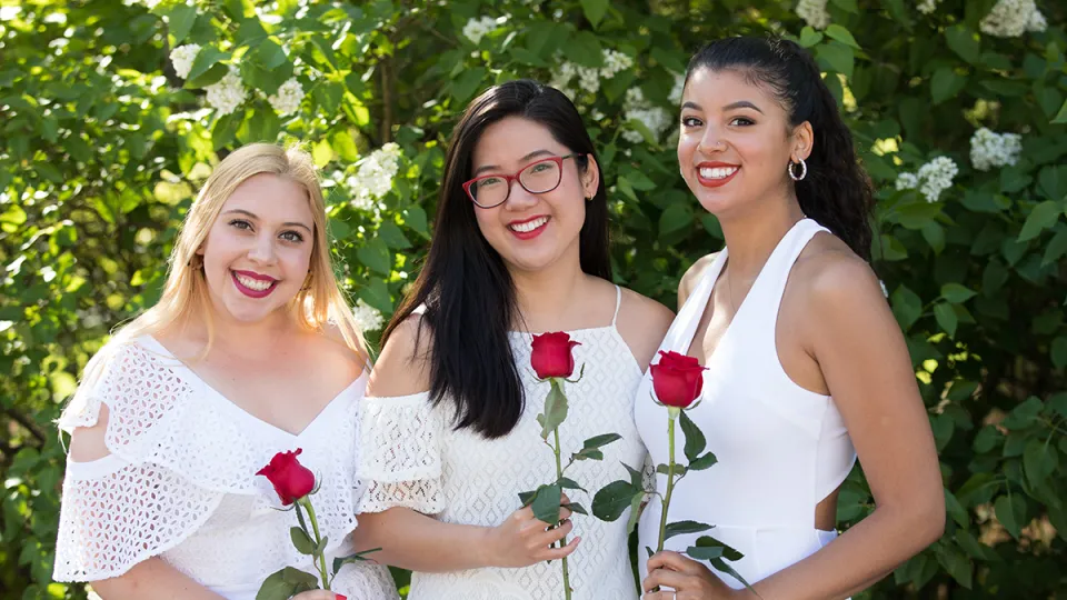 Three students holding red roses on Ivy Day