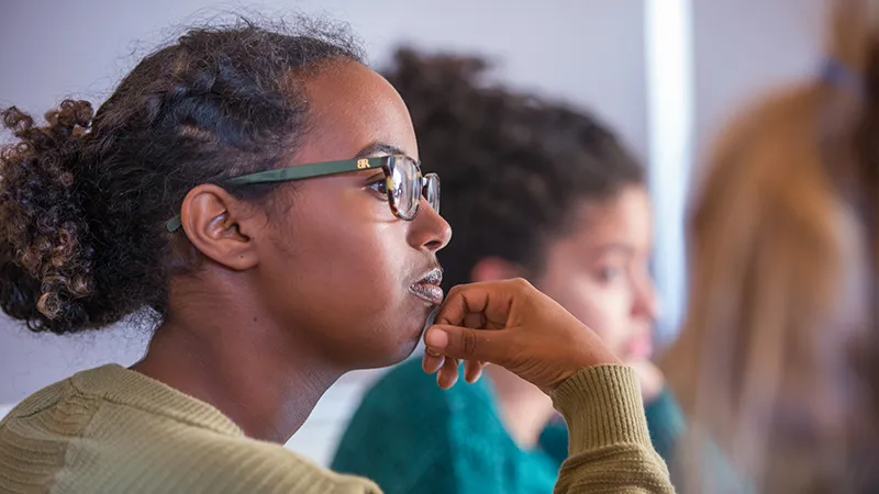 Student holding hand to face, listening intently in class